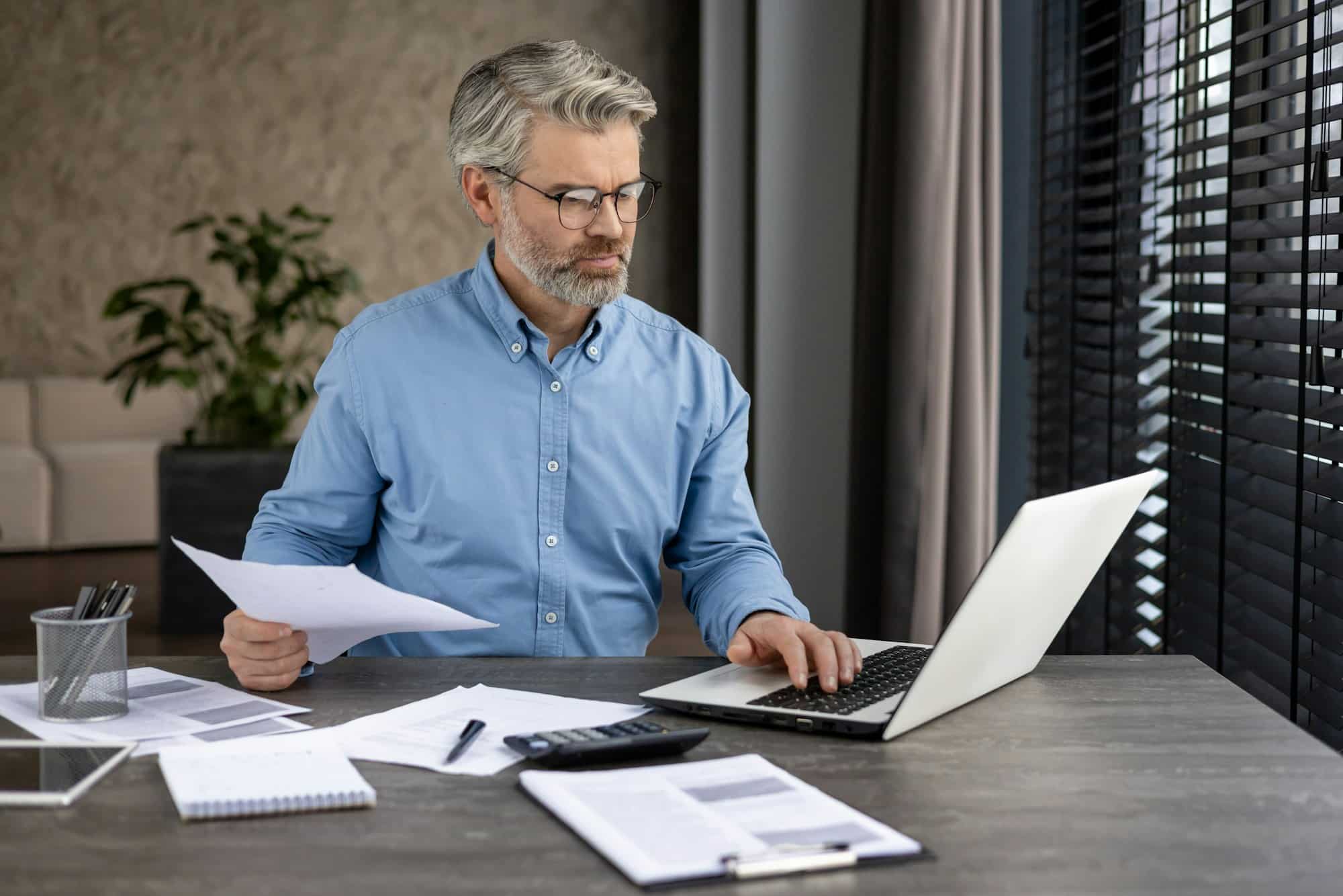 Mature businessman working at desk on laptop with documents in modern office